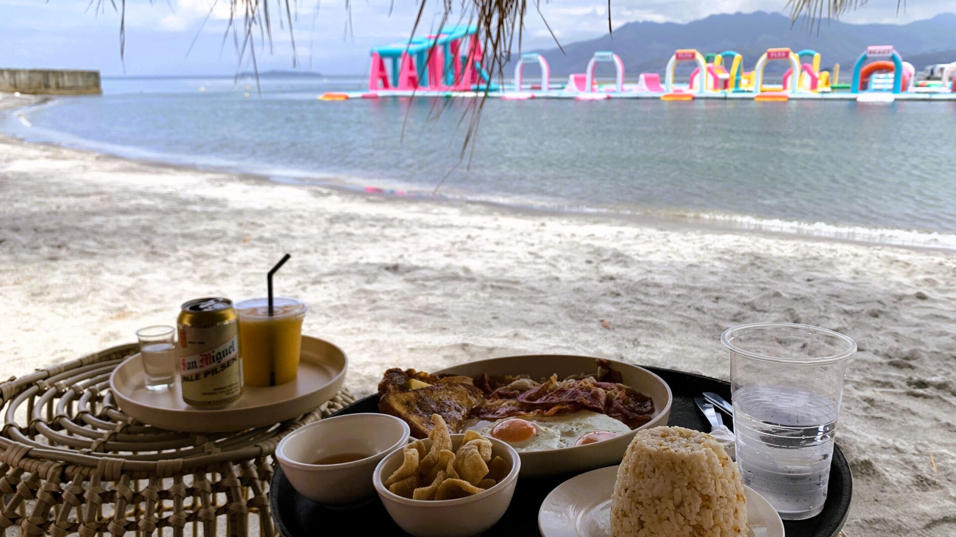 フィリピン・スービックにあるInflatable Islandのビーチエリア。日よけの下、料理を楽しみながら水上アトラクションと海を眺める風景