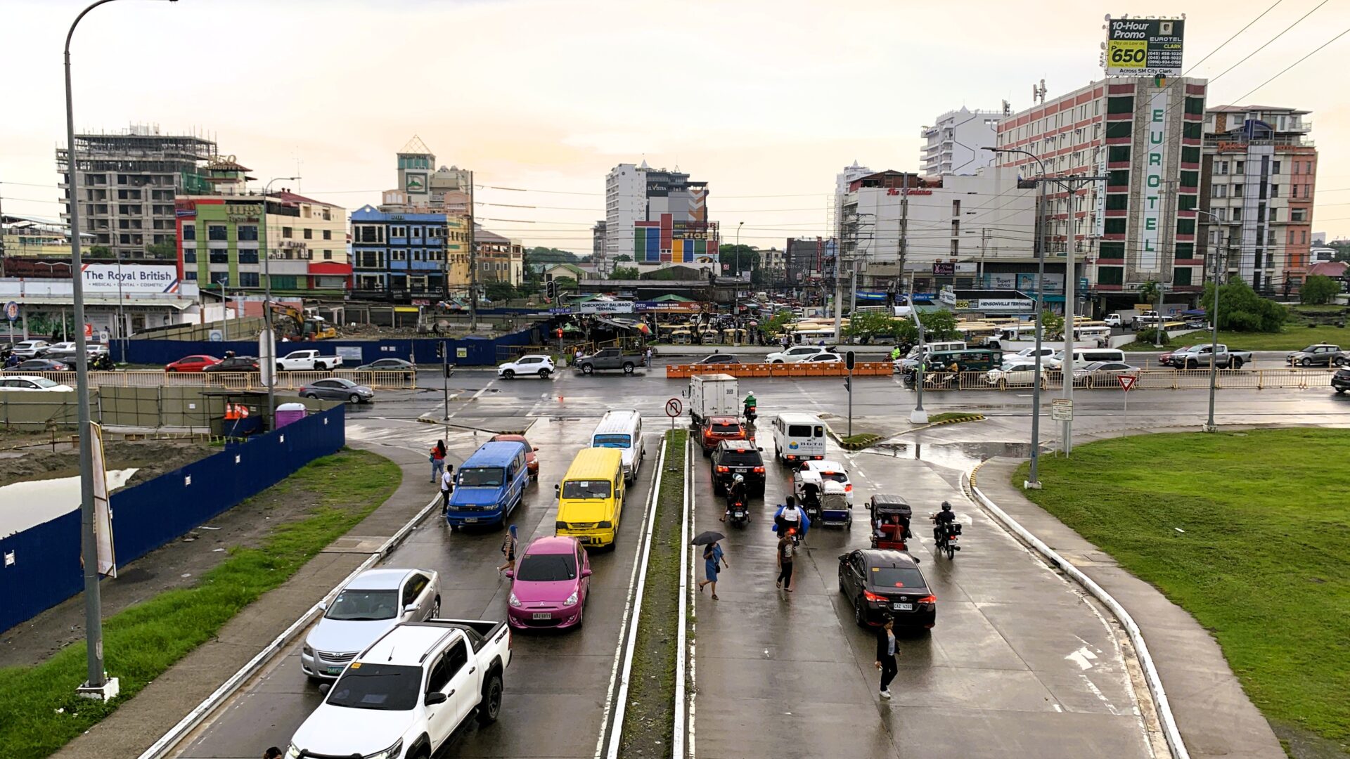 フィリピン・アンヘレスの歩道橋から見た街の景色。中央に2本の道路が伸び、突き当りにもう1本の道路がある。雨で濡れた路面に車やバイクが行き交い、ローカルな建物や水たまりも見える