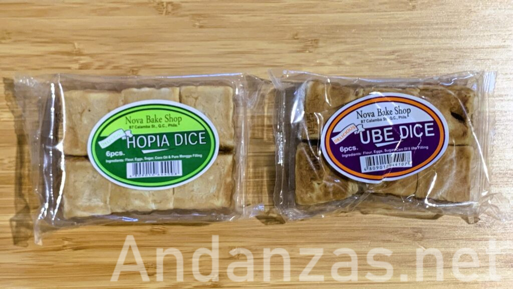 竹製のテーブルに置かれたウベダイスとオピアダイスのお菓子。紫の楕円形ラベルに「UBE DICE」と書かれた透明な袋に、さいころ型のウベダイスが6個詰められている