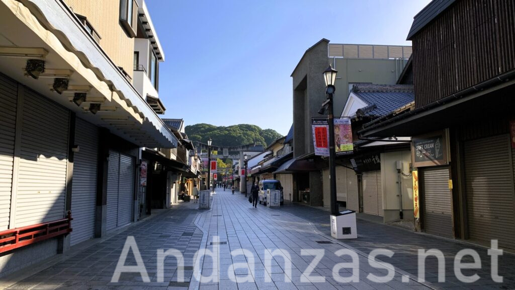 早朝の太宰府天満宮の参道。晴れた日、石畳が敷かれ、両脇に並ぶ店舗はほとんど閉まっている。観光客も少なく、静かな雰囲気が漂う時間帯。