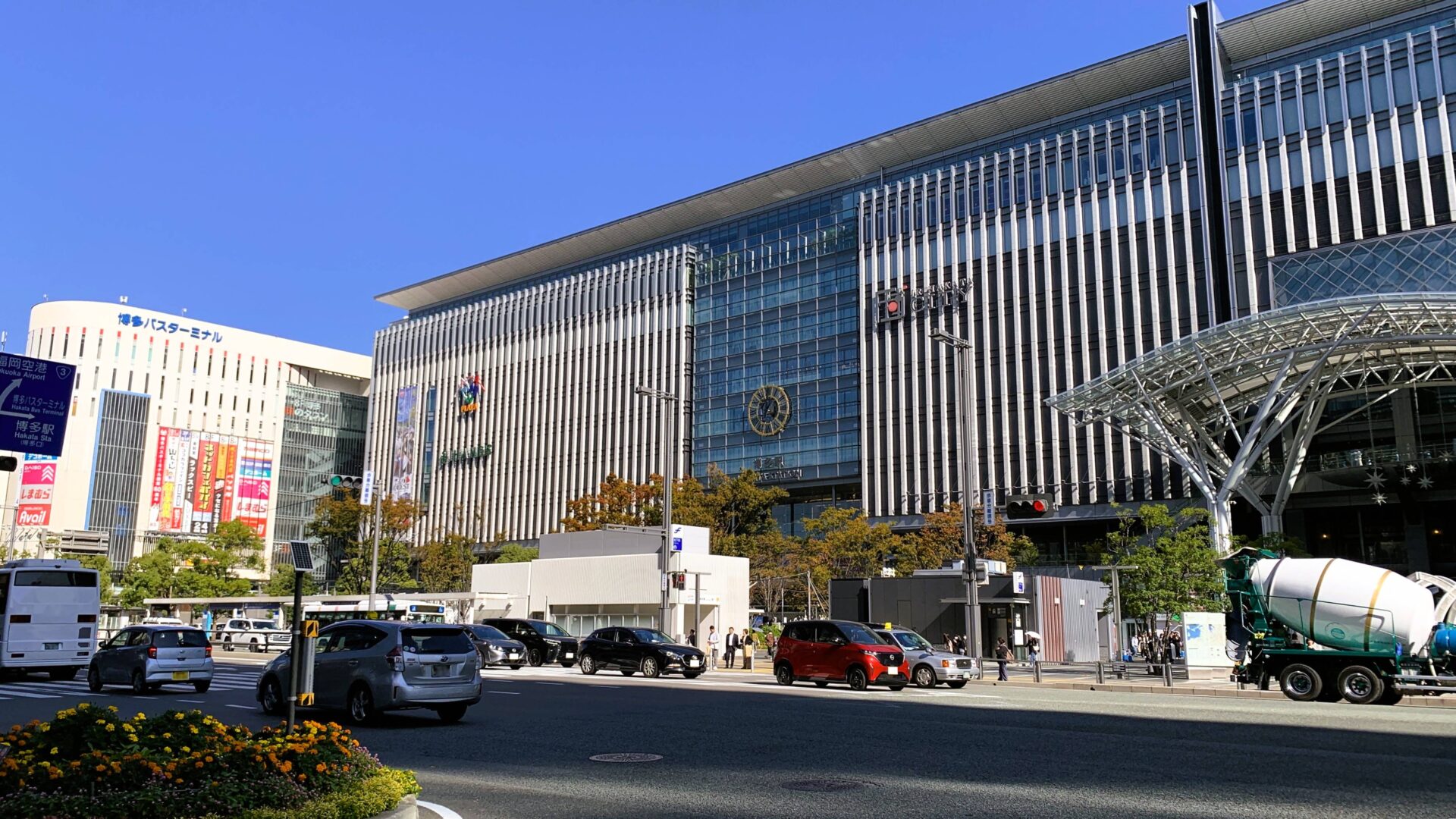 福岡・博多駅の駅ビルを撮影。奥に博多バスターミナルが見え、手前の道路には程よく車やバスが通り、快晴の青空が広がる都会的な風景。