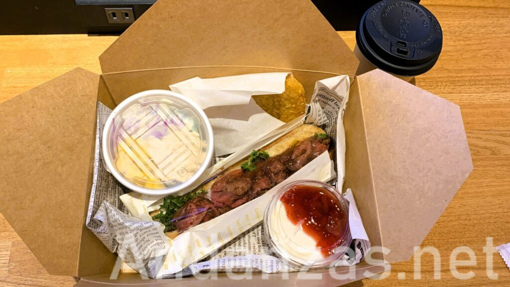 福岡・博多のATORI COFFEEの朝食。ローストビーフサンド、チキンサラダ、イチゴジャム入りヨーグルト、ポテトの揚げ物が入った箱。右上にはコーヒーがカップに入っている。木のテーブルに並べられた朝食セット。