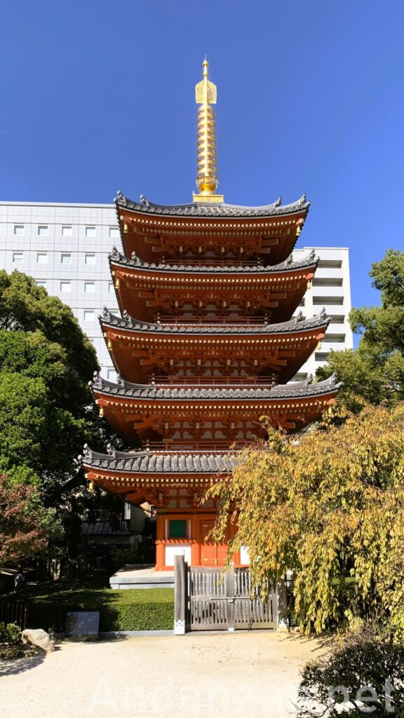 福岡・東長寺の五重塔。朱色の五重塔と青空のコントラストが際立ち、左右に木々、背景にビルが見える静寂な景色。