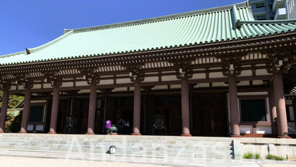 福岡・東長寺の本堂。石の階段の上に巨大な建物があり、頑丈な柱に支えられた屋根は薄緑色。内部は薄暗く、外は晴れた青空が広がる。