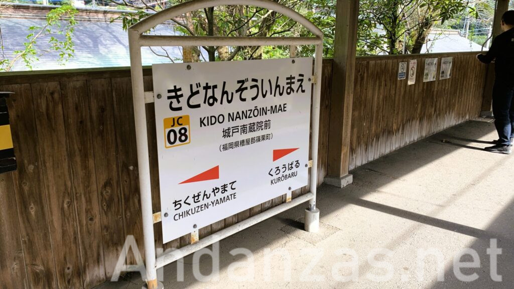 城戸南蔵院前駅の駅名看板。白地にひらがなで「きどなんぞういんまえ」と大きく書かれ、漢字と英語表記もある。駅の壁は木製で、上部には風景が見え、床には日差しが差し込んでいる。