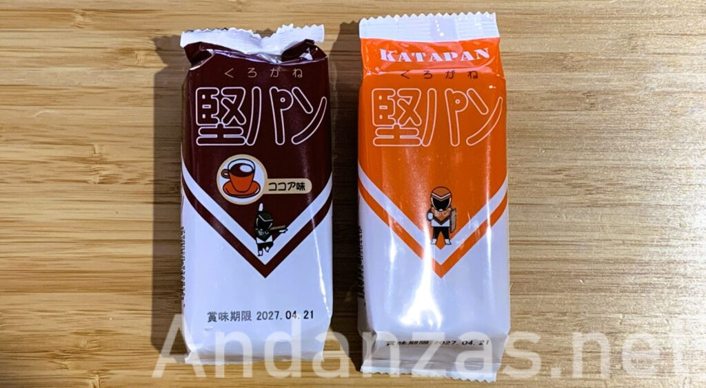 くろがねの堅パンココア味とプレーンが並んだ写真。ココア味は白地に茶色のパッケージ、プレーンはオレンジ色のパッケージ。どちらも上部に「堅パン」の文字が大きく書かれている。