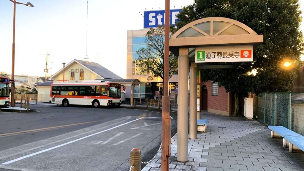 神奈川県大雄山駅前のバスロータリー早朝の様子。屋根付きバス停があり、1番乗り場には道了尊最乗寺の看板が立っている。右側には待機スペース、左側にはロータリーが広がる人がいない静かな風景である。