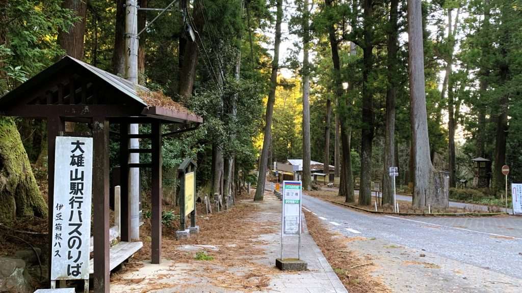 神奈川県最乗寺最寄りバス停道了尊を撮影したものである。山中に位置し、周囲は杉の木に囲まれている。右側にアスファルトの道路、左側に木製ベンチがあり、屋根がかかるバス停には大雄山駅行きののりば看板が設置されている。