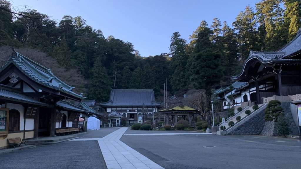 神奈川県最乗寺の境内を早朝に撮影した一枚。青空が広がるが日差しはなく、人影もない。広大な敷地に中央奥の僧堂と左の書院が見え、周囲の木々が静寂な雰囲気を作る。