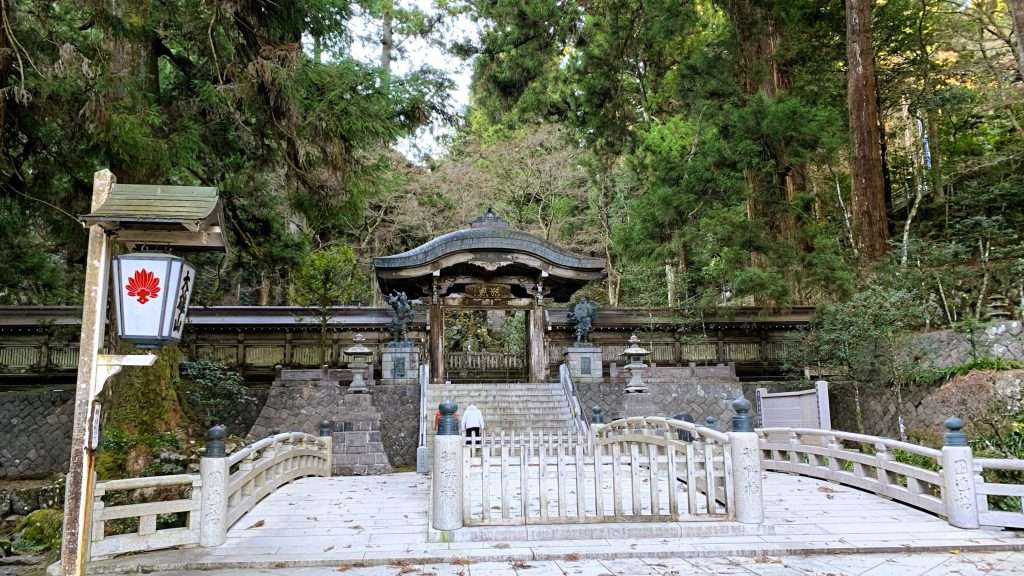 神奈川県最乗寺の結界門と御供橋。木製の門の両側に天狗像が配置され、石橋である御供橋が門前に架かる。橋の両脇には圓通橋が並び、周囲の木々が囲む中、一人の人が歩いている落ち着いた風景である。