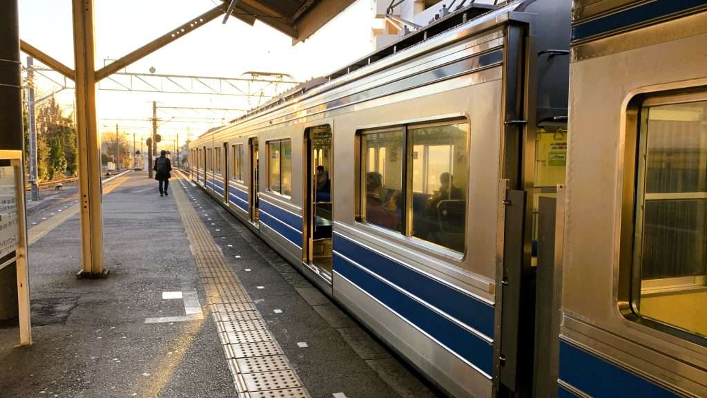 伊豆箱根鉄道大雄山線の大雄山駅ホームを朝に撮影した風景である。右側には銀色の車体に青いラインが入った電車が停車し、左側には駅ホームが続く。遠くには背を向けて歩く男性の姿が見え、車内には数人の乗客が確認できる。