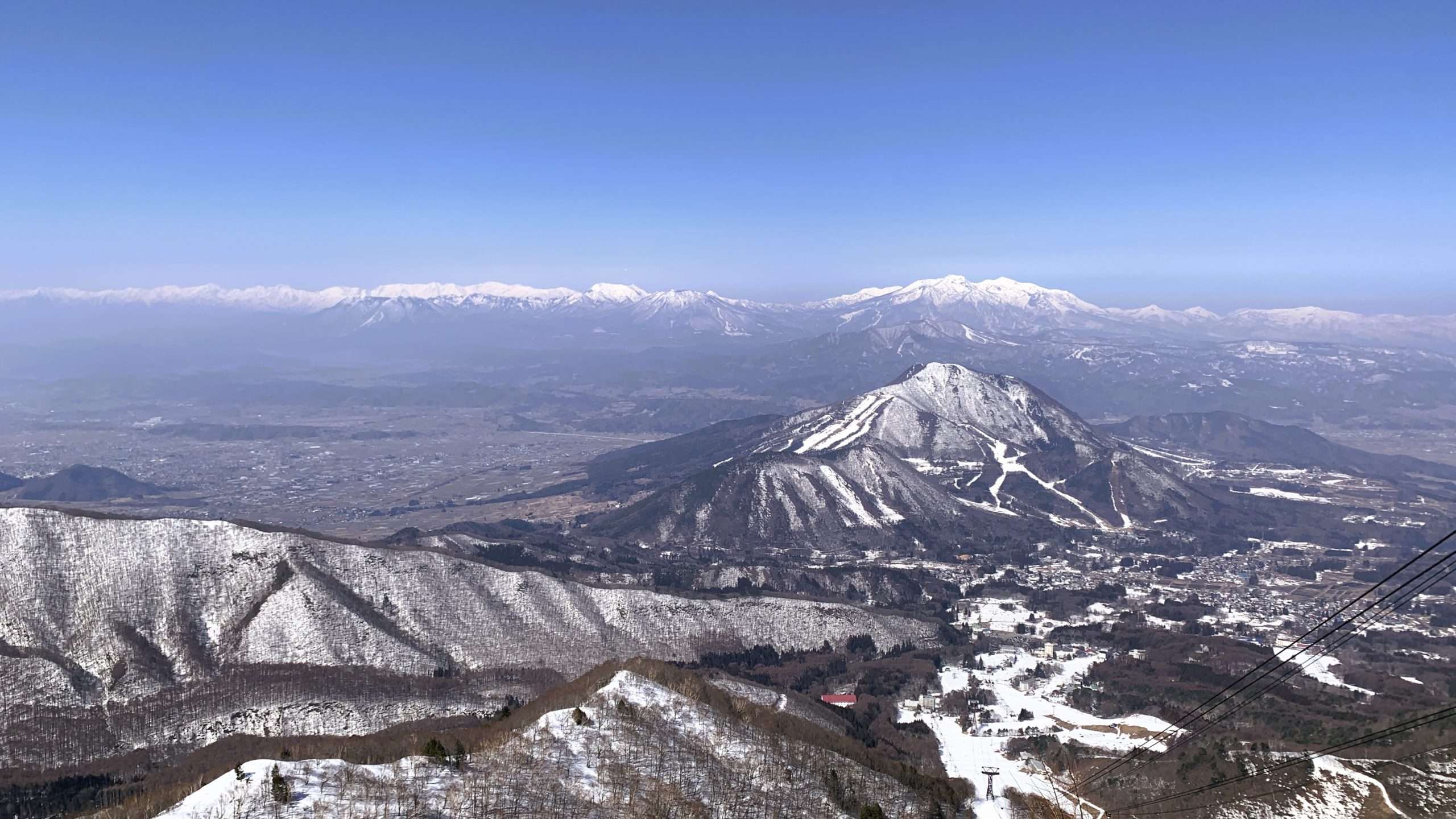 北志賀竜王スキーパークのSORA terraceロープウェイ山頂から見渡す冬の雪景色。手前にゲレンデ、奥に雪を抱く山々と中央アルプスの雄大な山脈が広がり、青空の下で自然の美しさが際立つ景観。