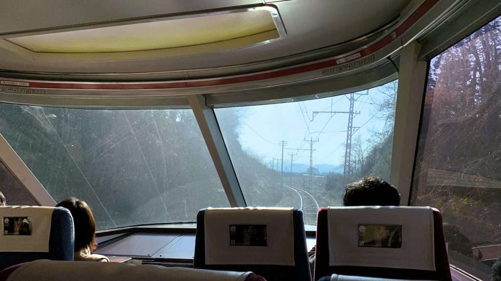 長野電鉄特急ゆけむり号の前面展望席からの眺め。旧小田急ロマンスカー車両の大きな窓からカーブする線路と森林、遠くに山と空が広がる臨場感ある車窓風景。