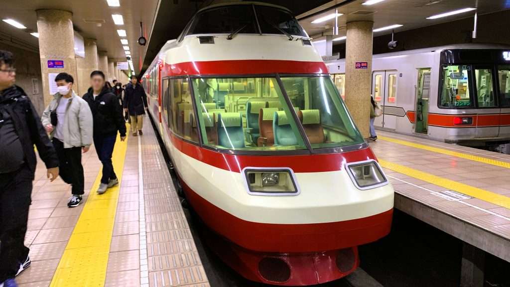 長野駅ホームで長野電鉄特急ゆけむり号を前方から撮影。元小田急ロマンスカー車両の特徴的な先頭デザインと大きな前面窓から見える座席。左側ホームを行き交う乗客と右側に停車する普通列車が写る駅構内の風景。