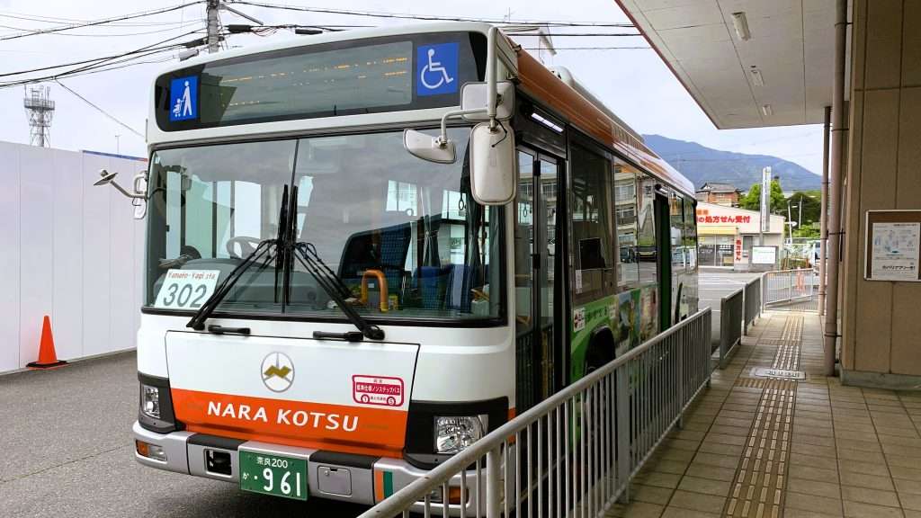奈良県五條市の五条バスセンターに停車する奈良交通バス。白とオレンジのカラーリング、302系統と大和八木ステーション行きの英字表示、運転手や乗客が見えない落ち着いた駅前交通風景。