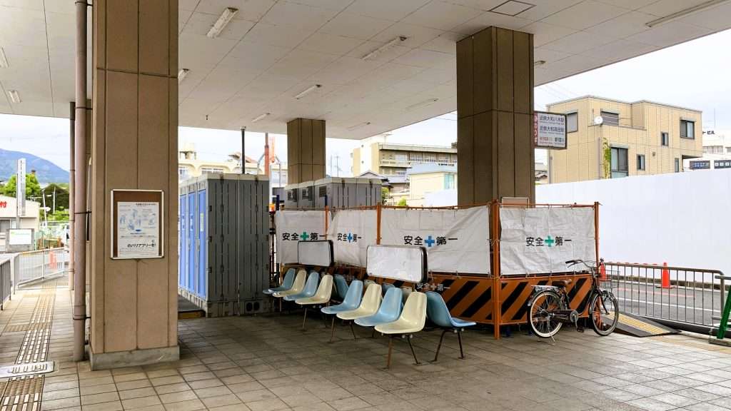 奈良県五条バスセンターの様子、白と水色のベンチ、仮設トイレと工事用バリケードが設置された構内、石柱で支えられた屋根構造、曇天で人のいない静かなバスセンターの景観。
