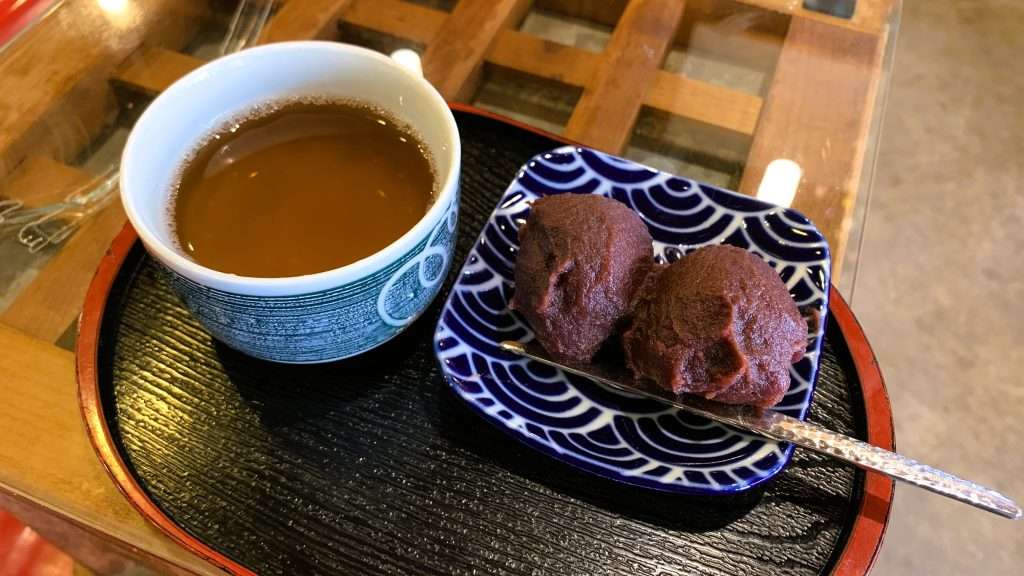 京都・天橋立名物の知恵の餅を撮影。やわらかい餅にあんこを包んだ和菓子が皿に2個並び、金属製の菓子楊枝が添えられ、左側にはほうじ茶が置かれた天橋立名物の甘味。