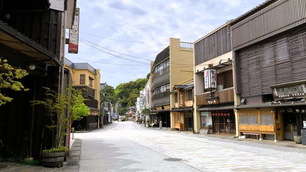 早朝の京都・天橋立の商店街を撮影した風景。石畳の通りの両側に低層の店舗が並び、右側には知恵の餅を提供する店が見える。人影のない静かな朝と曇り空が広がる観光地の街並み。