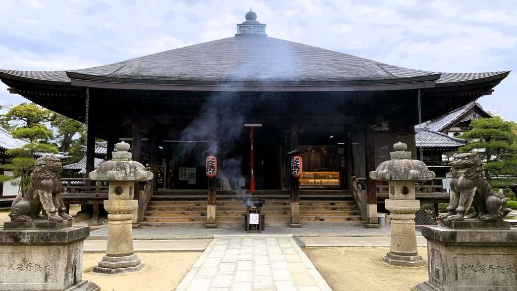 早朝の京都・天橋立智恩寺の文殊堂を正面から撮影した風景。香炉から線香の煙が立ち上り、左右に狛犬と石灯籠が並ぶ、曇り空の下で人影のない厳かな雰囲気の寺院景観。