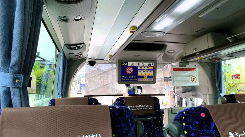 丹後海陸交通の天橋立から大阪行き高速バスの車内を撮影。3列目の座席から前方を望み、青い柄のシートに茶色のヘッドカバーが付いた車内。前方ディスプレイには「次は宮津駅」の案内が表示された、空いた車内風景。