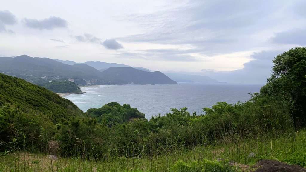 静岡県下田市・白浜海岸を丘の上から望む朝の風景。濃い青色の海には白い波が立ち、曇り空の下、周囲を山々に囲まれた美しい伊豆の海岸景観。